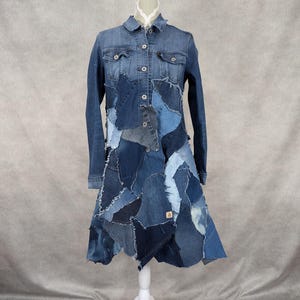 Peut inclure: Une longue robe en jean faite de tissu en jean patchwork. La robe a un devant boutonné et des manches longues. La robe est sur un mannequin blanc.