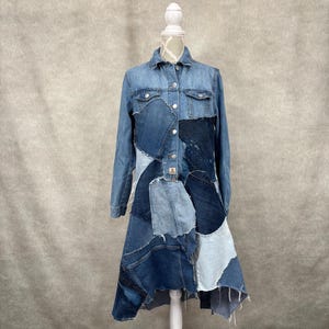 Könnte beinhalten: Ein langärmeliges Jeans-Hemdkleid mit einem Patchwork-Design aus verschiedenen Blautönen von Denim-Stoff. Das Kleid verfügt über einen Kragen, eine durchgehende Knopfleiste, zwei Brusttaschen und einen asymmetrischen Saum mit ausgefransten Kanten.
