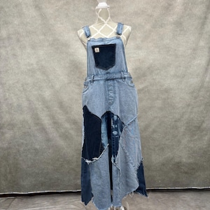 Puede incluir: Vestido de peto vaquero azul claro con diseño patchwork. El vestido presenta un bolsillo de peto y tirantes ajustables. La falda tiene un diseño patchwork asimétrico en varios tonos de mezclilla azul. El vestido se exhibe en un maniquí.