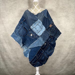 May include: A denim poncho made from repurposed blue jeans. The poncho is made of various shades of blue denim and has multiple pockets.