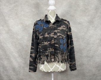 May include: A cropped camouflage jacket featuring a button-down front, long sleeves, and a frayed hemline. The jacket is decorated with two large, blue denim flower appliqués on the chest and includes two chest pockets with button closures.