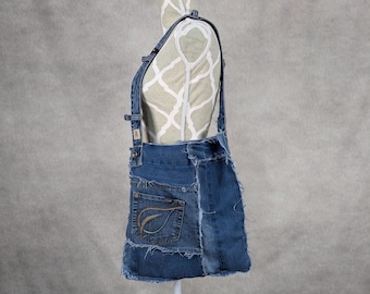 May include: A blue denim tote bag with a patchwork design. The bag has a long strap and a leaf-shaped design on the front.