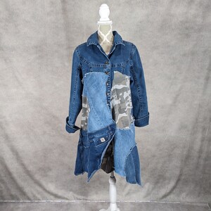 May include: A long denim jacket with a patchwork design featuring different shades of blue denim and a camouflage print. The jacket has a collar, long sleeves, and a button closure.