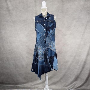 May include: A denim dress made from patchwork denim fabric. The dress has a sleeveless bodice and a flared skirt. The dress is on a white mannequin.