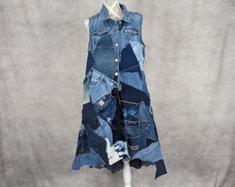 May include: A long denim vest made from patchwork denim fabric. The vest has a sleeveless design and a pointed hemline. The vest is displayed on a white mannequin.