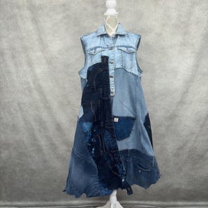 May include: A sleeveless denim dress in various shades of blue, displayed on a white mannequin. The dress features a patchwork design with pockets and seams, creating a unique, textured look. The dress has a collared neckline and button-down front.