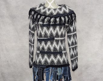 May include: A black and white knitted sweater with a fringe trim around the neckline and a denim fringe trim around the hem.