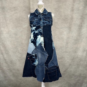 May include: A sleeveless denim dress with a patchwork design. The dress features a collared neckline, button-down front, and various shades of blue denim patches. It is displayed on a white mannequin.