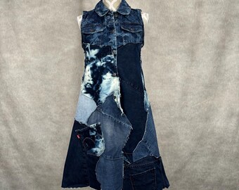 May include: A sleeveless denim dress with a patchwork design. The dress has a collared neckline, button-down front, and various shades of blue denim patches. It is displayed on a white mannequin.