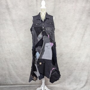 May include: A long denim vest made from repurposed denim pieces. The vest has a patchwork design with different shades of blue and black denim. The vest has a collar and button closure.