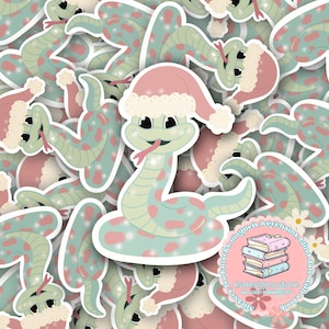 May include: A collection of stickers featuring a cartoon snake wearing a Santa hat. The snake is light green with pink spots and a red tongue. The hat is pink with white trim. The stickers are from ksdesigns store.