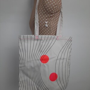 May include: White canvas tote bag with black wavy lines and two bright red circles.