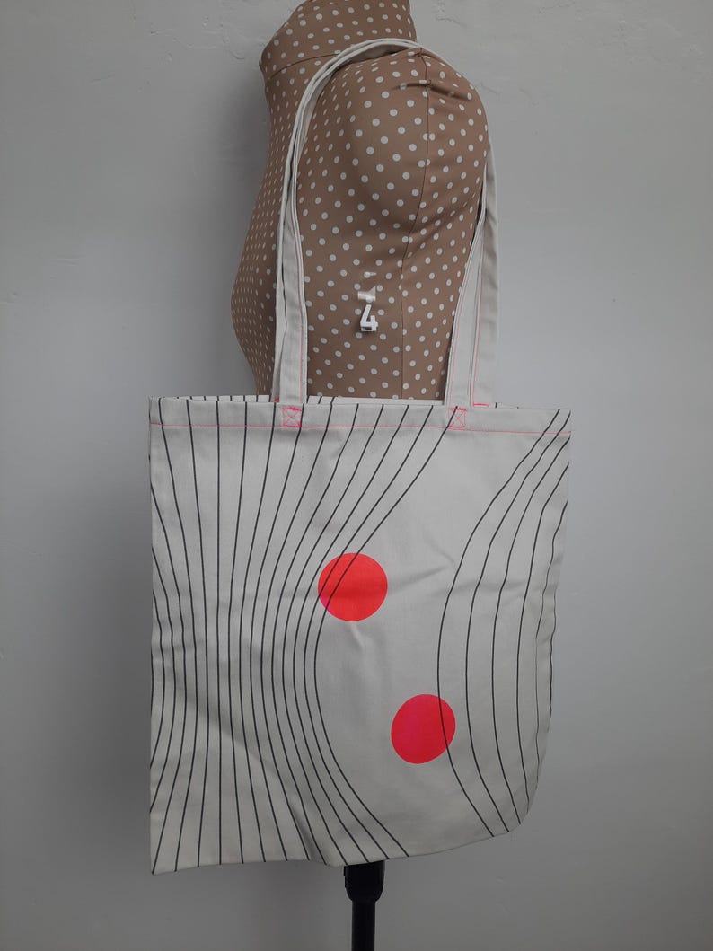 May include: White canvas tote bag with black wavy lines and two bright red circles.
