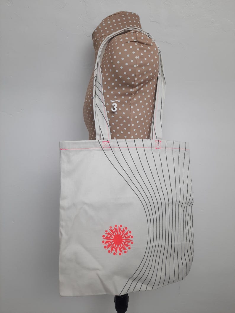 May include: White canvas tote bag with black and pink stripes and a red and pink flower design. The bag has two long straps.