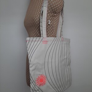 May include: White tote bag with black stripes and a pink flower design. The bag has the text "Grazie Chic" printed on it.