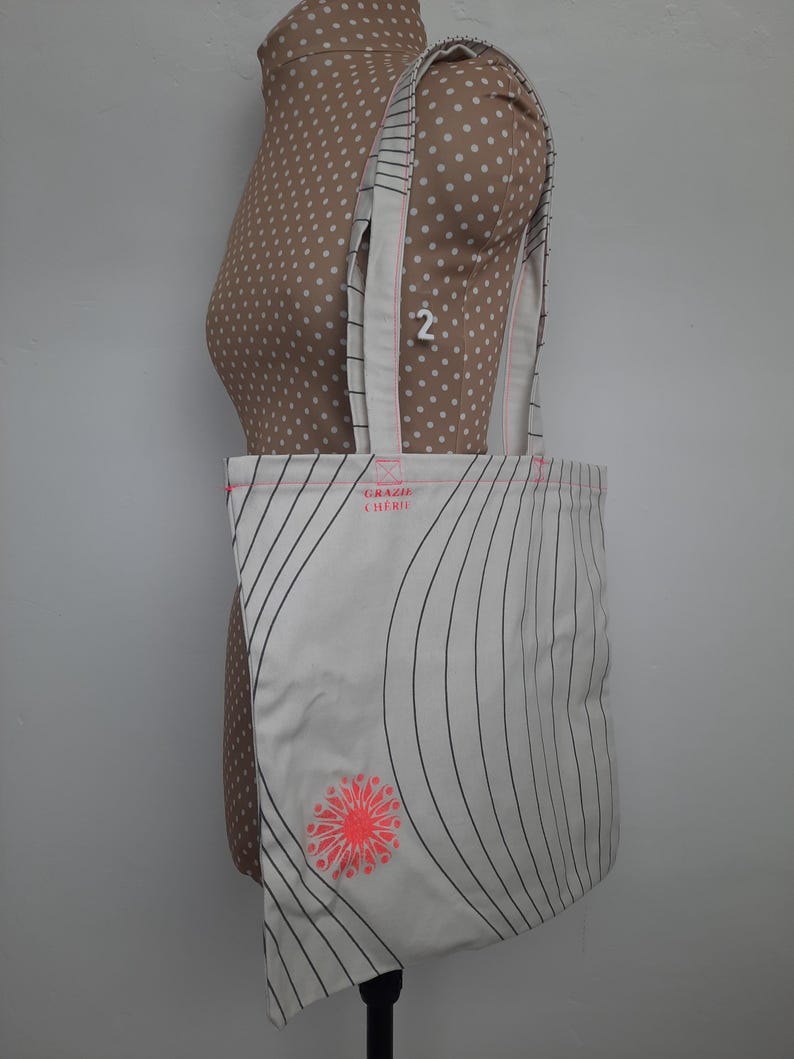 May include: White tote bag with black stripes and a pink flower design. The bag has the text "Grazie Chic" printed on it.