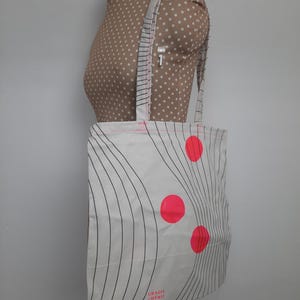 May include: White canvas tote bag with black wavy lines and three bright pink circles. The bag has a pink handle and the text "Grazia Cherry" printed on the bottom.