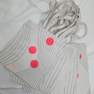 May include: A stack of white tote bags with black stripes and pink circles. The bags have the text "FINISTERRE" printed on them.