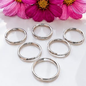 May include: Six circular silver-toned metal split rings arranged in a triangular formation. Each ring features a continuous wire loop design with a small gap for opening, providing a polished, reflective surface finish for various attachment uses.
