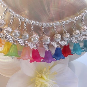 May include: A string of nine silver angel charms with pearl beads and translucent flower-shaped pendants in rainbow colors.