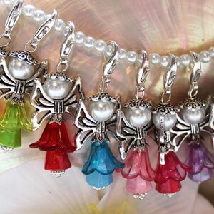 Peut inclure: Un ensemble de sept breloques d'anges colorés avec des ailes argentées et une perle. Chaque breloque est dotée d'un fermoir à homard argenté pour l'attacher à un sac, un porte-clés ou tout autre objet.