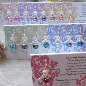 Può includere: Una collezione di ciondoli a forma di angelo in argento con perline di diversi colori. I ciondoli sono esposti su carte con un motivo floreale. Le carte includono il testo "Schön, dass Du da bist" e "Benedict Maximilian" con una data.