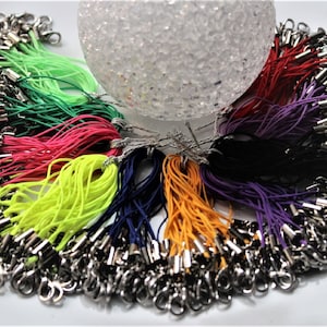 Puede incluir: Una colección de cordones de cuerda de colores con cierres de langosta plateados. Los cordones están dispuestos en círculo, con los cierres hacia afuera. Los colores de los cordones incluyen verde, rosa, amarillo, azul, naranja, morado, rojo y negro.