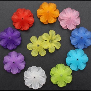 May include: Assortment of ten colourful plastic flower-shaped embellishments. The flowers are in shades of purple, blue, green, yellow, pink, orange, and white.