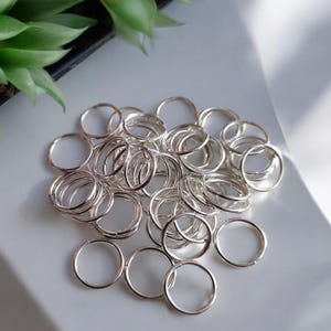 Puede incluir: Un montón de anillas de salto plateadas, un tipo de hallazgo de joyería utilizado para conectar cadenas, cordones y otros componentes de joyería.