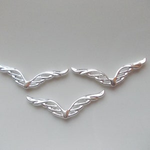 Può includere: Tre ali in metallo argentato con un design delicato e intricato. Le ali sono curve e hanno una punta appuntita.