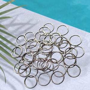 Könnte beinhalten: Eine Ansammlung zahlreicher silberfarbener Metall-Buchringe, die in einem Haufen angeordnet sind. Jeder Ring hat eine kreisförmige Form mit einer sichtbaren Naht, wodurch die Ringe geöffnet und geschlossen werden können. Die Oberfläche ist glatt.