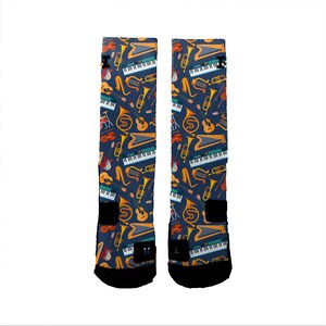May include: A pair of blue athletic socks with a colorful pattern of musical instruments, including trumpets, drums, guitars, and a keyboard.