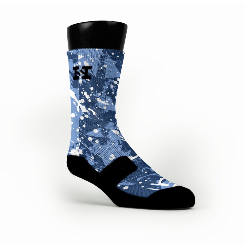 Puede incluir: Calcetines deportivos azules y blancos con un dise&ntilde;o de salpicaduras de pintura. Los calcetines tienen un logotipo negro en el lateral y una correa negra en el tobillo.