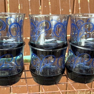 May include: Six clear glass tumblers with a blue floral design. The glasses are stacked in pairs.