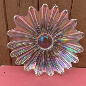 May include: A clear iridescent glass serving dish shaped like a flower with a scalloped edge. The dish has a centre circle with a rainbow iridescent finish.