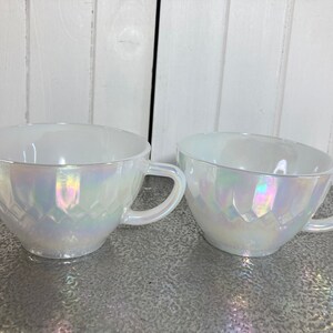May include: Two white iridescent teacups with a diamond pattern. The cups have a glossy finish and are made of glass.