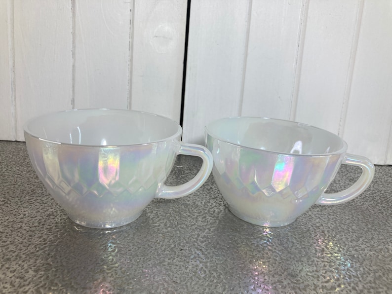 May include: Two white iridescent teacups with a diamond pattern. The cups have a glossy finish and are made of glass.