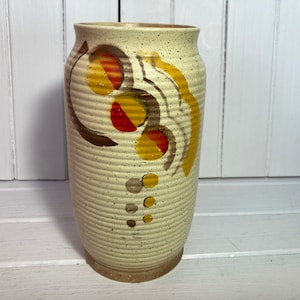 May include: A white ceramic vase with a speckled texture and a geometric design in shades of brown, yellow, and red.