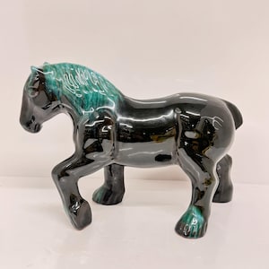 Op de afbeelding: Een zwart keramiek paardenbeeldje met een turquoise glazuur. Het paard heeft een vloeiende manen en staart.