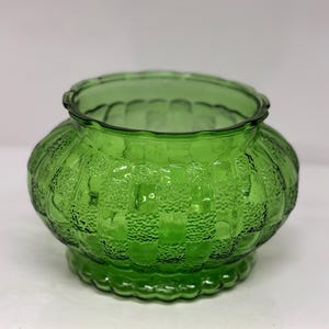 May include: A green glass bowl with a textured, ribbed design. The bowl has a rounded shape and a scalloped rim.
