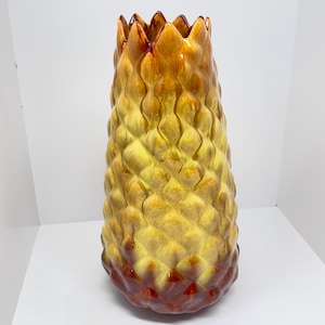 Puede incluir: Un jarrón de cerámica amarillo y naranja con una superficie texturizada que se asemeja a una piña. El jarrón tiene una abertura ancha y una base redondeada.