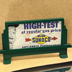 May include: A green and white sign with the text "HIGH-TEST at regular gas price" and a yellow and red arrow pointing to the right with the text "BLUE SUNOCO" and "ANTI-KNOCK PERFORMANCE".