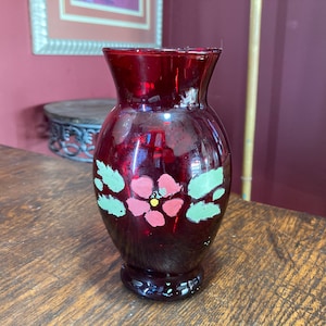 Peut inclure: Un petit vase en verre rouge peint à la main avec un motif floral vert et rose.