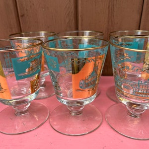 May include: Set of six clear glass drinking glasses with gold trim and a turquoise and orange design. The glasses have a short stem and a wide bowl.