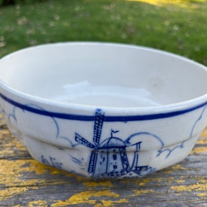 May include: A white ceramic bowl with a blue rim and a blue and white windmill design. The bowl is decorated with clouds and has a scalloped edge.