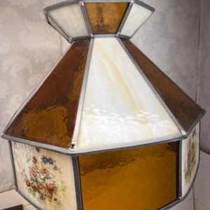 Puede incluir: Una l&aacute;mpara colgante de vidrio emplomado con un dise&ntilde;o geom&eacute;trico marr&oacute;n y blanco. La l&aacute;mpara tiene un patr&oacute;n floral en la parte inferior.