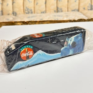 May include: A blue and white Coca-Cola branded plastic case with a polar bear holding a bottle of Coca-Cola. The case has the words "Always" and "Coca-Cola" printed on it. The case has a white mountain scene in the background. The case has the words "Pulse" and "Tone" printed on it.