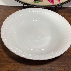 May include: White ceramic bowl with a fluted rim and a gold trim. The bowl is empty and has a smooth, glossy finish.