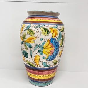 Könnte beinhalten: Eine weiße Keramikvase mit einem bunten Blumenmuster und gestreiften Akzenten. Die Vase ist mit gelben, blauen, grünen und rosa Blumen und Blättern verziert.