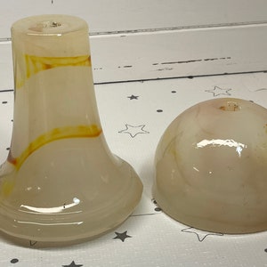 May include: Two-piece glass object with a light beige and orange swirl design. The larger piece is vase-shaped with a flared base. The smaller piece is dome-shaped. Both pieces have a hole at the top.